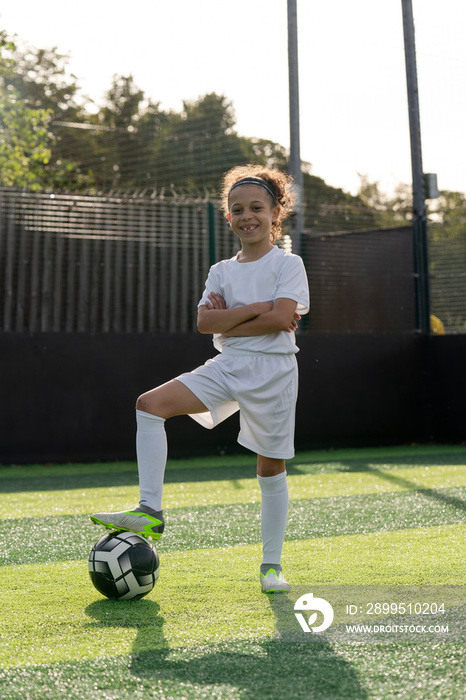 Portrait of girl (6-7) with ball on soccer field