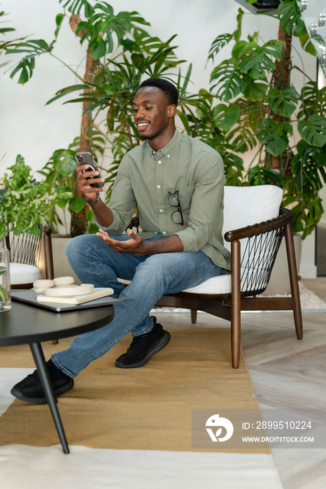 Young man with smartphone sitting in office lounge