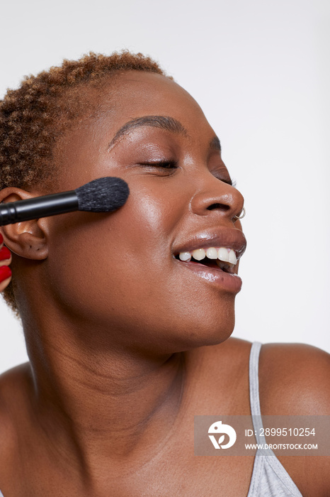 Studio portrait of smiling woman applying blush