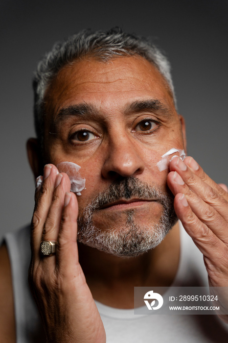 Portrait of man applying face cream against gray background