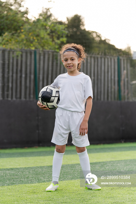 Portrait of girl (6-7) with ball on soccer field