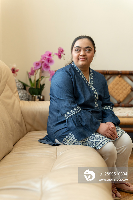 Portrait of young woman with down syndrome sitting on sofa at home