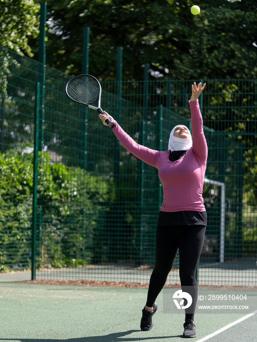 UK,Sutton,Woman in headscarf playing tennis in park