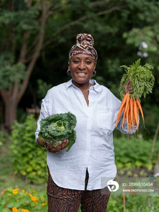 Portrait of smiling mature woman holding vegetables in allotment