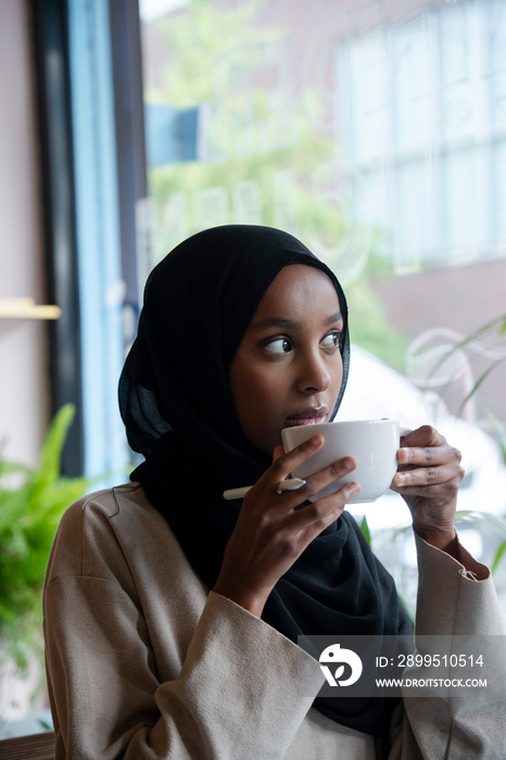 Young woman in hijab drinking coffee in cafe