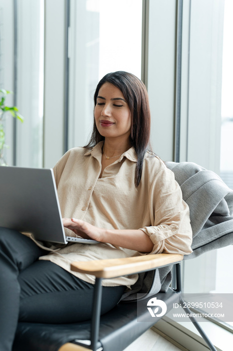 Businesswoman with laptop sitting in office lobby