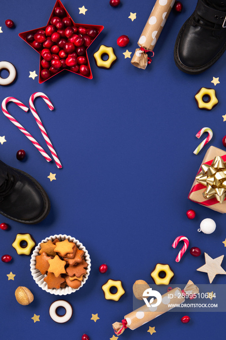 Christmas card with children’s shoes, sweets, candy, gingerbread cookies, gifts on blue background, top view.   Saint Nicholas Day, 6 December.