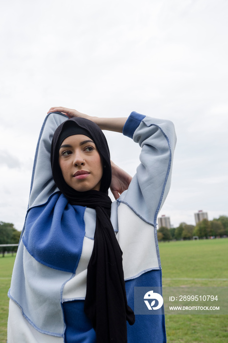 Portrait of woman in hijab stretching arm in park