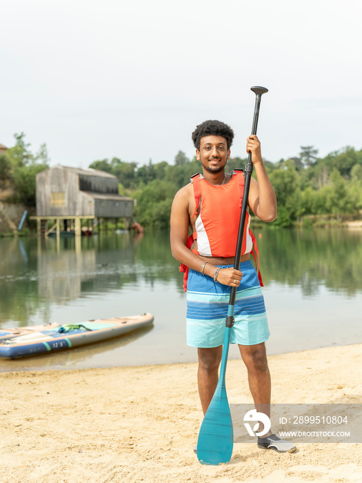 Portrait of young man standing with oar on beach