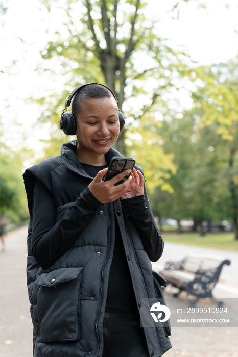 Smiling woman with headphones and smart phone in park