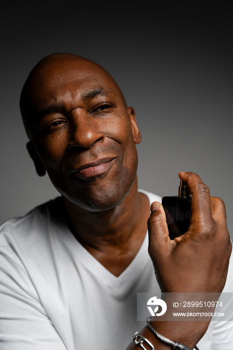 Portrait of man putting on perfume against gray background