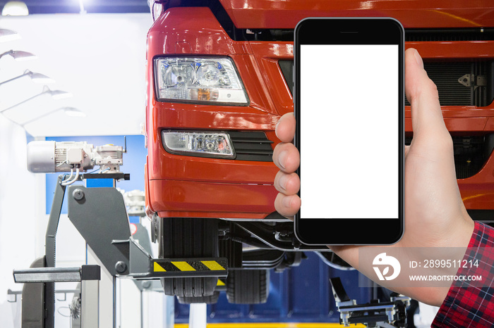 Hand with phone on a background of truck on a lift in a car service