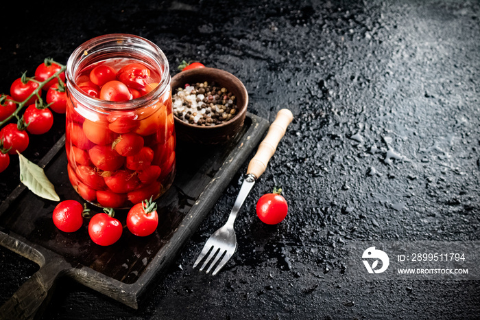 Pickled tomatoes in a glass jar on a cutting board.