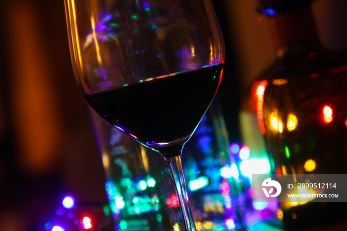 Close up of red wine glass with bottles of alcohol and colorful electric light