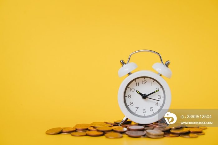 white analog clock with blurred pile of coins on grunge yellow background for business and finance concept , time for savings money concept, banking and business idea