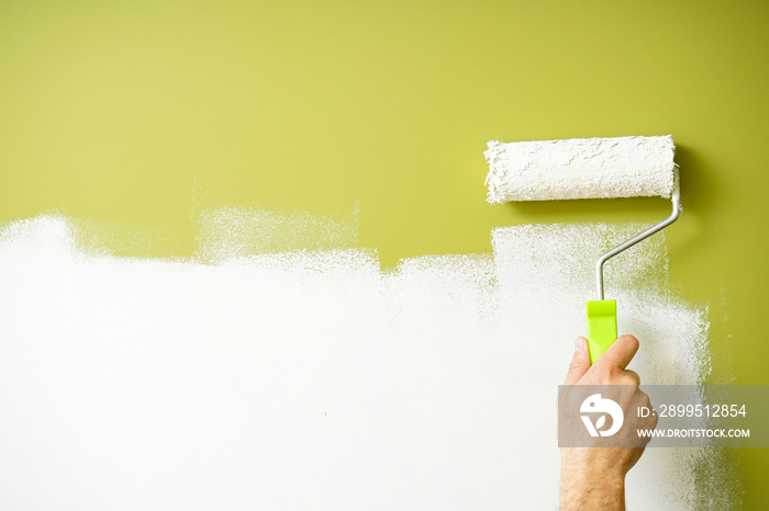 Paint roller in the hand of a man repainting the wall, space for text.