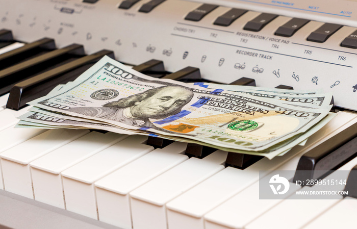 US Dollars lie on the piano keys. Payment for the concert, profit from performing musical works_