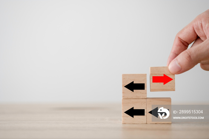 Hand putting red arrow on wooden cube which opposite direction with black arrow. Disruption and different thinking for discovery new technology  and new business opportunity concept.