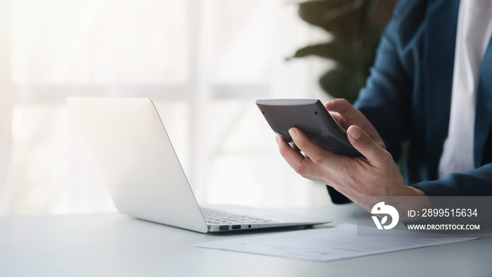 Businessman using a calculator to calculate numbers on a company’s financial documents, he is analyzing historical financial data to plan how to grow the company. Financial concept.