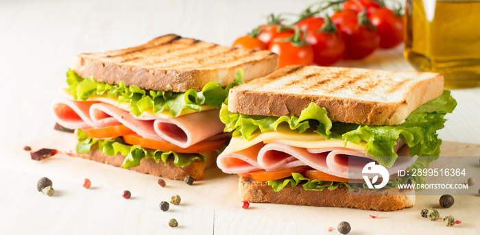 Close-up photo of a club sandwich. Sandwich with meat, prosciutto, salami, salad, vegetables, lettuce, tomato, onion and mustard on a fresh sliced rye bread on wooden background. Olives background.