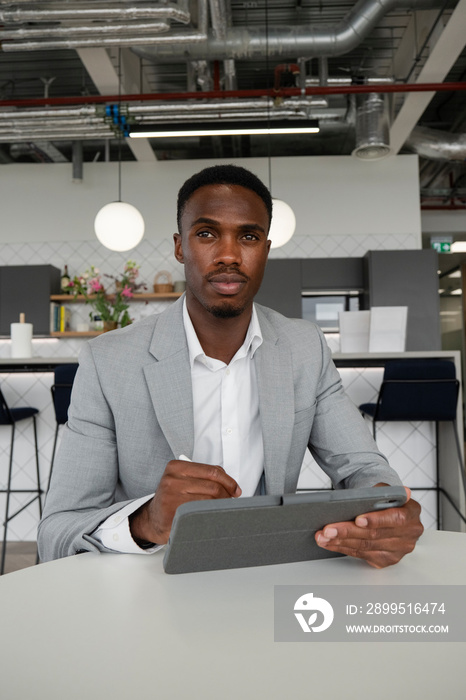 Portrait of young businessman using digital tablet in office cafeteria