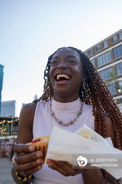 Laughing young woman holding hot dog