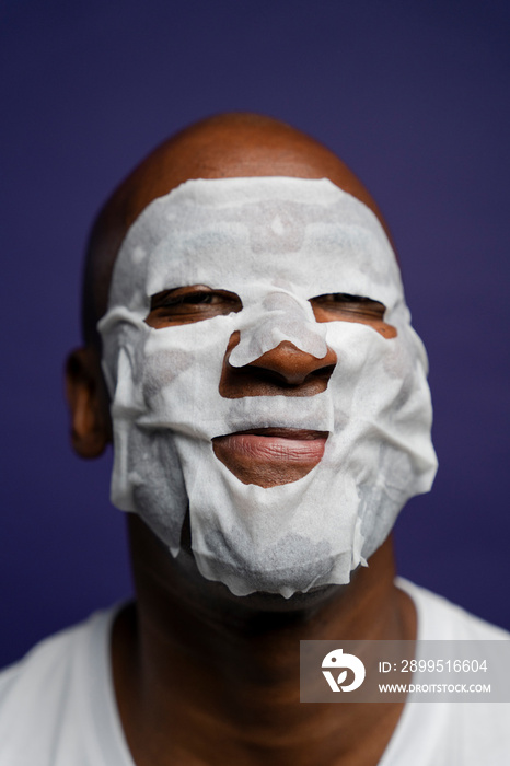 Portrait of man in facial mask against purple background