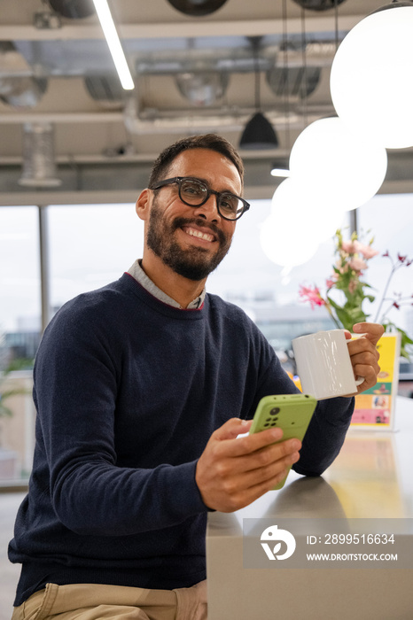 Portrait of man using smart phone in office kitchen