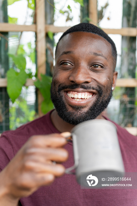 Portrait of smiling man holding metal mug in urban garden