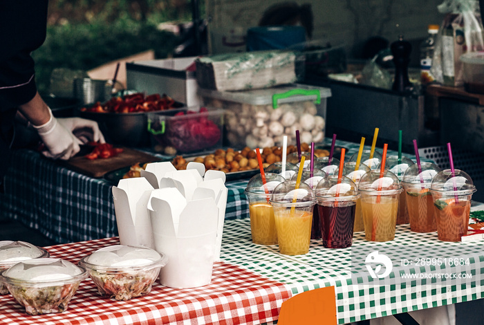 colorful lemonade on table and fast food paper boxes, space for text. street food festival. drink bar at reception, catering outdoors. summer picnic. cocktails in plastic cups with straws