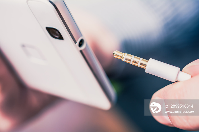 Headphone Jack Of A White Mobile Phone Next To A Headset Cable