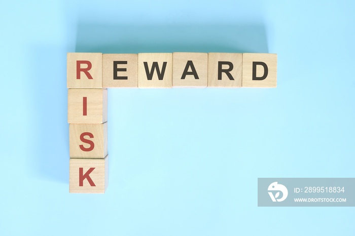 Risk and reward business concept. Wooden block crossword puzzle flat lay in blue background.