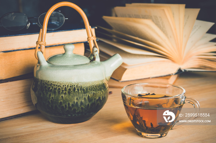 A cup of tea with tea pot and reading book on table