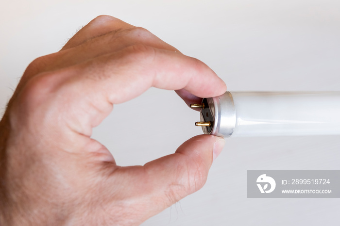 Male hand holds with fingers end with contacts of fluorescent lamp, close-up. A man examines the contacts of the lamp.