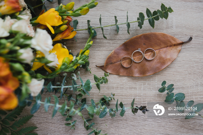 Botanic bridal chic. Bouquet with silk ribbons, wedding rings and engagement ring on wooden background.