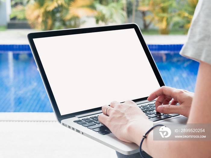 Young women working by the swimming pool. Female remote worker writing code, study, surfing the internet during summer. Close up of hand typing on computer laptop with white blank screen.