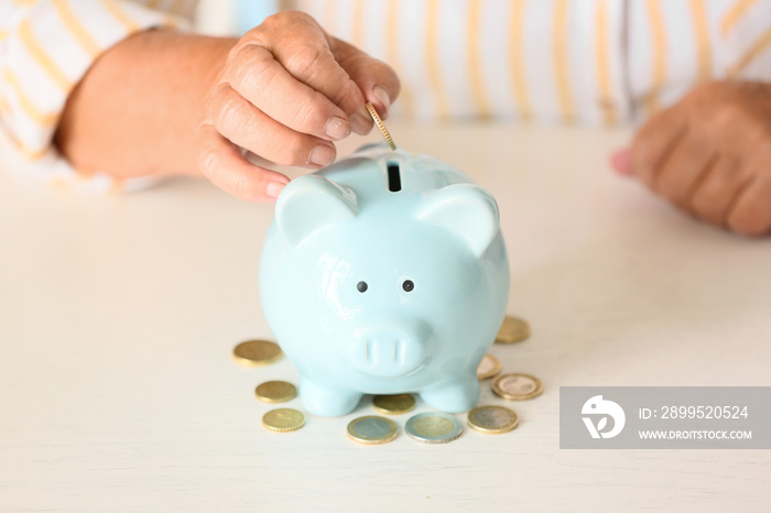 Senior woman putting coin into piggy bank at table. Concept of pension