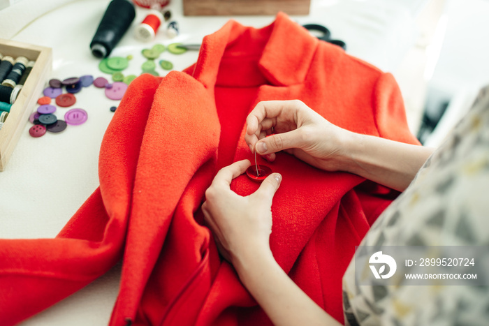 a seamstress sews a button on a red coat on white table