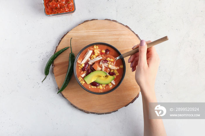 Woman eating tasty chicken enchilada soup from bowl on table