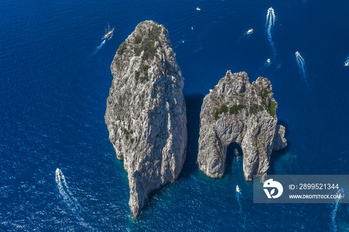 Aerial drone shot view of faraglioni limestone crags in summer in Tyrrhenian sea with yachts off Capri Island