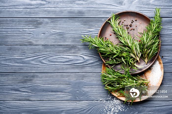 Plates with fresh rosemary and spices on dark wooden background