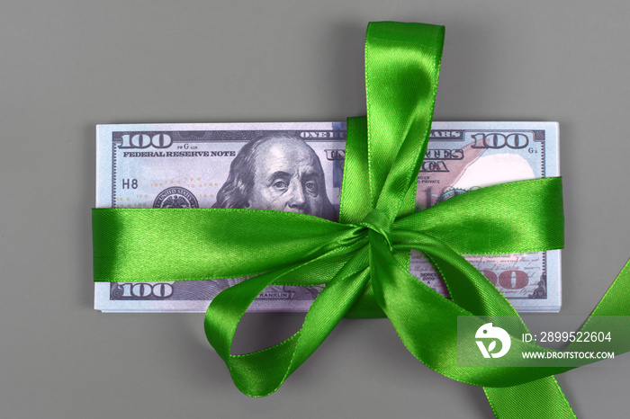 Hundred dollar bill tied with green bow on grey background. Money, gift wrapped in green bow and ribbon, US currency, cash, business success, bonus, monetary prize, luck in the game concept