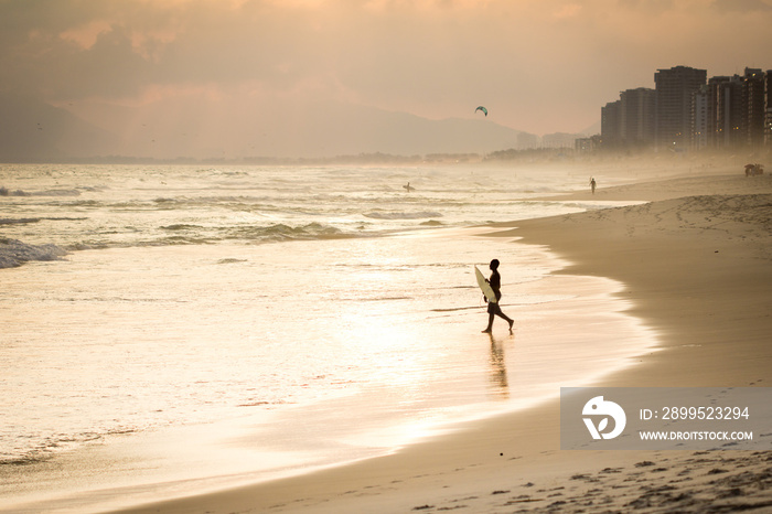 Silhouette of surfer walking on the beach during sunset