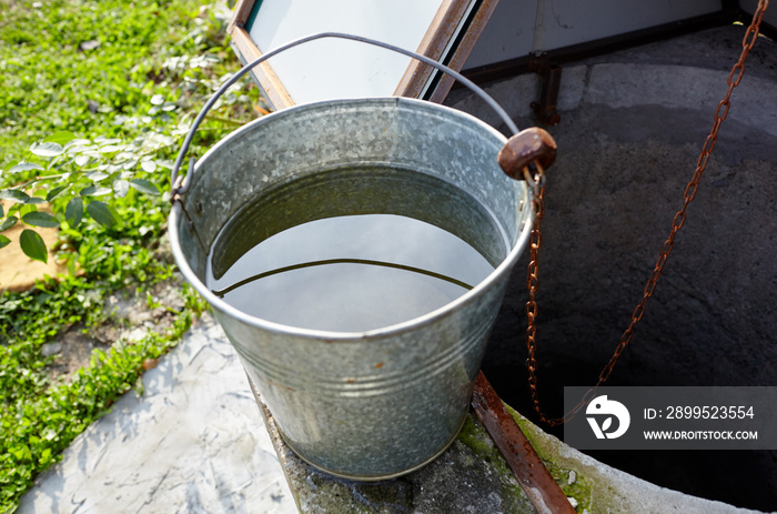 Metal bucket at draw-well in European village. Retro stone water well in rural area