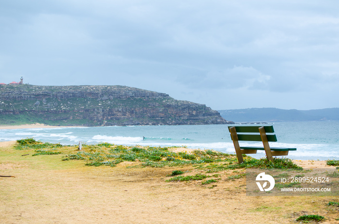 Green Park bench near the ocean, beach shows dark blue sea and horizon clouds sky day at Palm Beach, Northern Sydney, Australia.