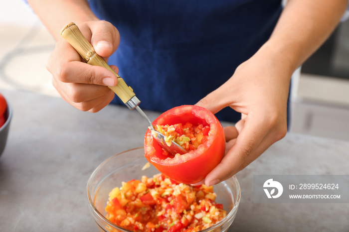 Woman preparing stuffed tomatoes at table in kitchen, closeup