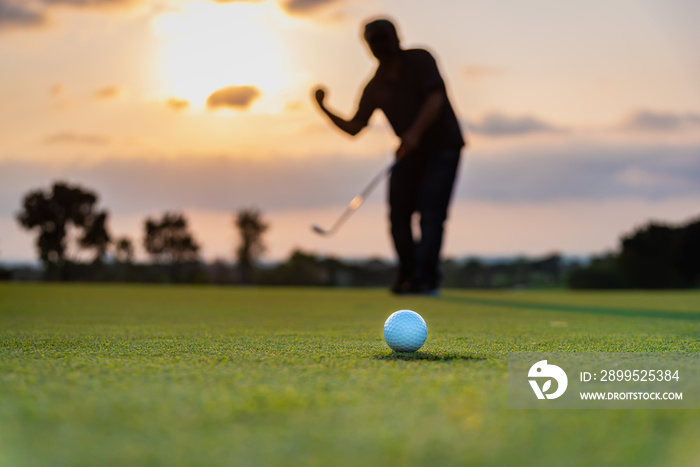 Silhouette golfer showing happiness when win in game , white golf ball on green grass of golf course with blur background.