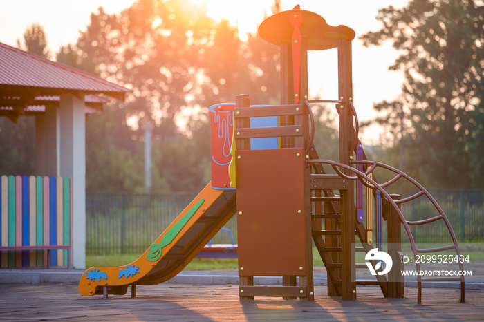 Nursery playground with colorful slides on soft rubber flooring with no children at sunset or sunrise.