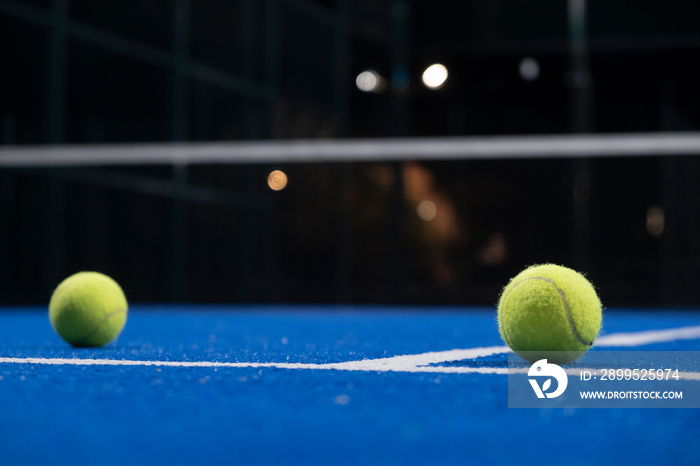 two balls on the surface of a blue paddle tennis court at night