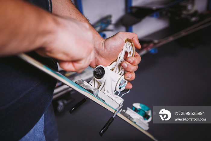 Theme tincture and repair ski equipment ski. Close-up of a Caucasian man’s hand use a hand-held screwdriver tool to tweak, twist bindings for ski boots in the workshop